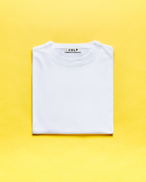 A folded white t-shirt featuring the CDLP brand label inside the neckline against a vibrant yellow background.