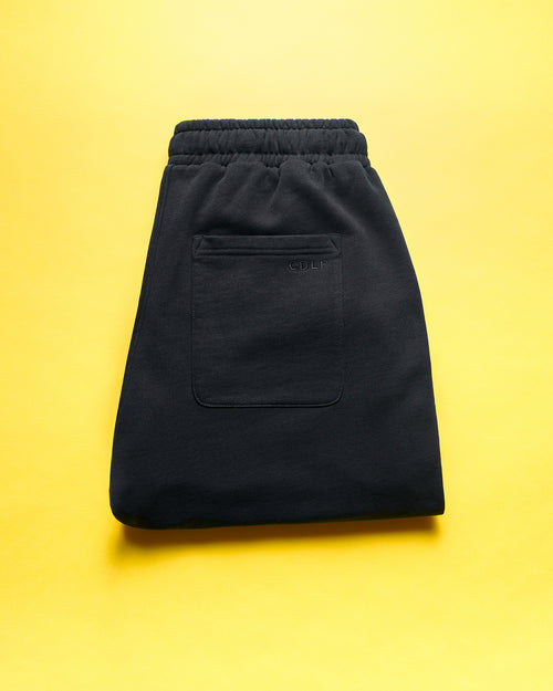 Black lounge shorts folded on a bright yellow background, showing the elastic waistband and back pocket with the CDLP logo.