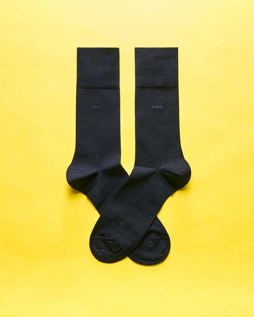 A pair of black socks laid flat and crossed over each other on a vibrant yellow background.