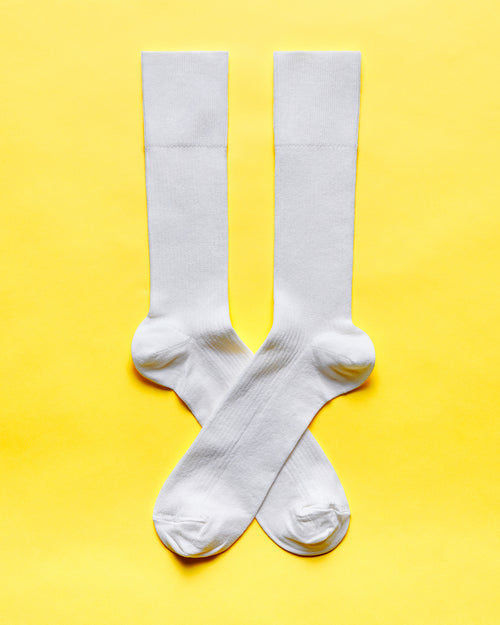 A pair of white socks laid out flat on a solid yellow background.