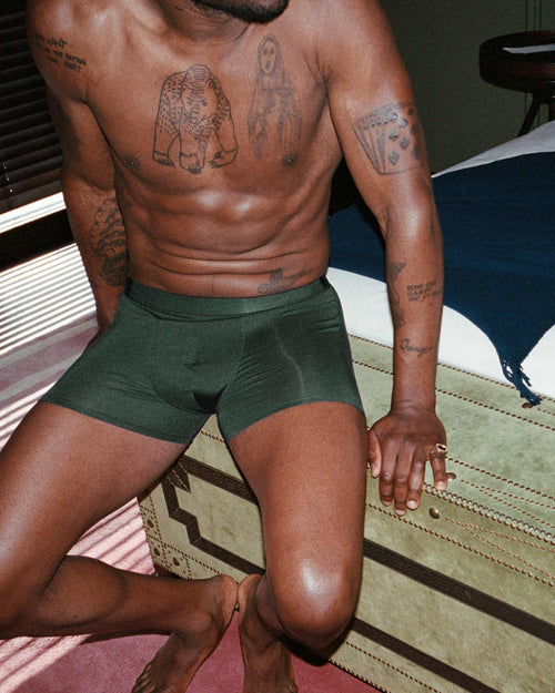 Marcus sitting on the bed wearing CDLP Lyocell Boxer Brief in Army Green
