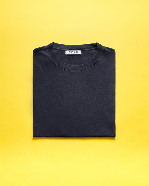 A folded dark t-shirt with a visible CDLP branded neck label on a yellow background.