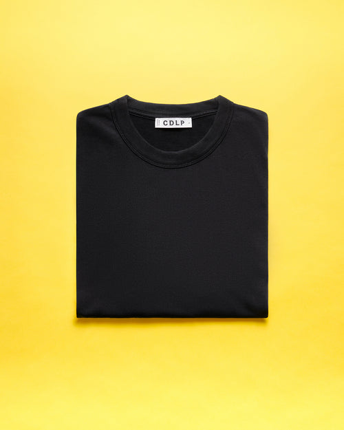 A folded black t-shirt with a visible CDLP brand label on a vibrant yellow background.