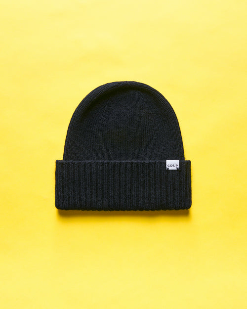 A black knit beanie with a folded brim and a small white CDLP brand label on a vibrant yellow background.