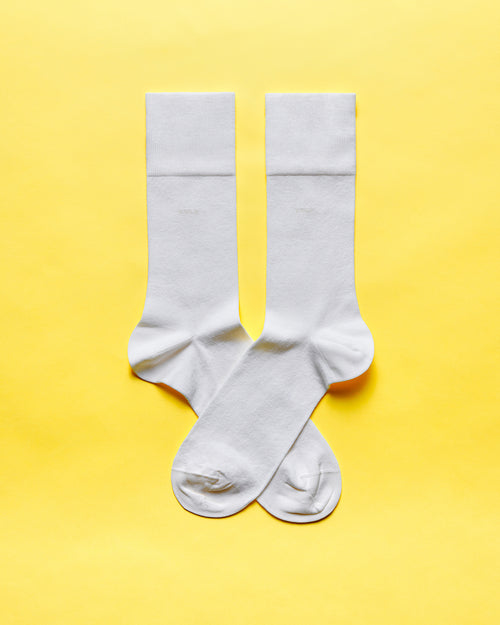 Two white socks displayed flat against a vibrant yellow background.