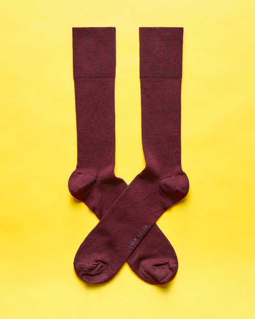 A pair of dark red ribbed socks arranged in a crossed position against a yellow background.