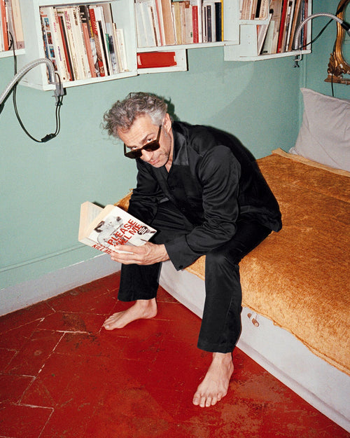 Francesco sitting on the bed reading a book wearing Home Trousers in Black