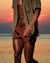 Sylla walking by the ocean wearing Swim Shorts in Rust